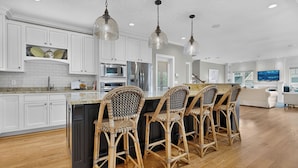 A modern kitchen with white cabinets, a central island with bar stools, stainless steel appliances, and pendant lighting. - Happy Holidays with Sea Breeze (Scarborough)