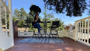 En träveranda med ett vitt räcke, två svarta stolar och ett litet bord.