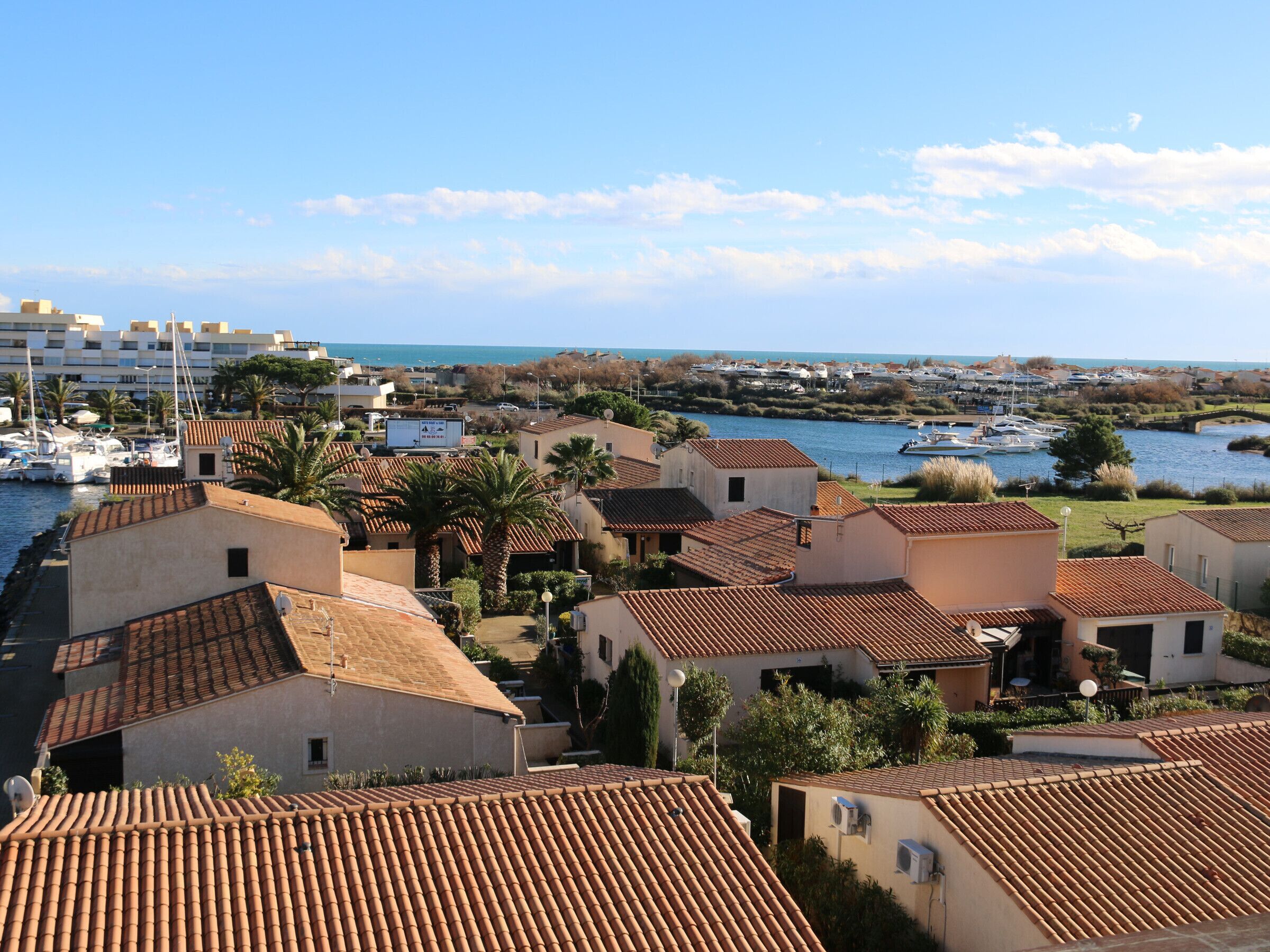 Eine Küstenwohngegend mit Häusern mit Terrakotta-Dächern, einer Marina mit Booten und freiem Blick auf das Meer.