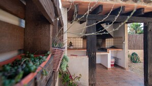 A covered outdoor kitchen area with a tiled floor, a wooden pergola, and potted plants. - VILLA JAVI (Riumar)