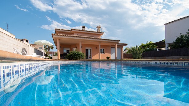 A swimming pool with clear blue water, a house with a tiled roof, and a clear sky. - VILLA JAVI (Riumar)