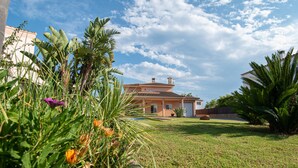 A house with a tiled roof, surrounded by a well-maintained lawn and various plants. - VILLA JAVI (Riumar)