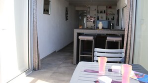 A dining area with a table and chairs, a kitchen in the background, and a window with curtains. - Air-conditioned apartment for 2 in Cap d'Agde (Cap d'Agde naturisme)