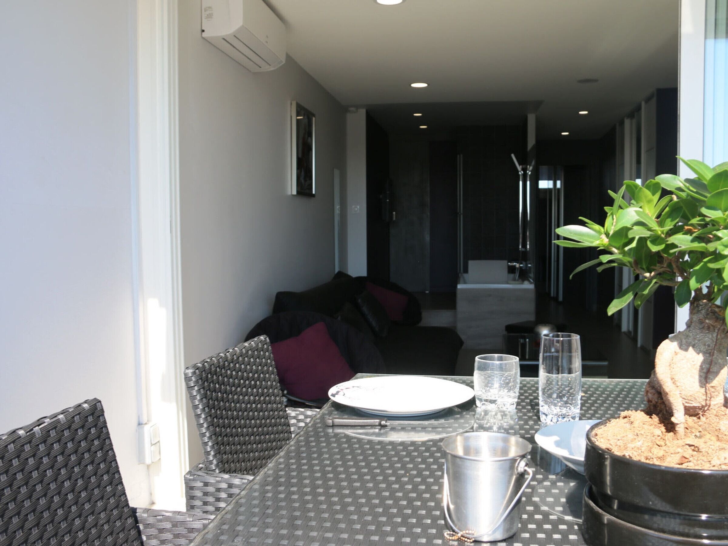 Un comedor con una mesa dispuesta para dos, una planta en maceta y vista al salón.
