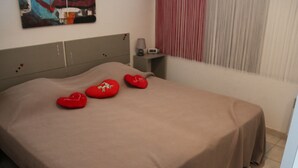 Ein ordentlich bezogenes Bett mit einer braunen Tagesdecke und drei herzförmigen roten Kissen.