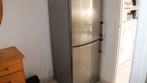 Eine kleine Küche mit einem Edelstahlkühlschrank, einem Holzschrank und einem gefliesten Boden.
