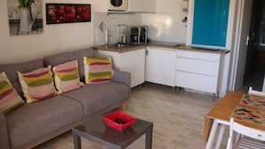 Un espace de vie compact comprenant un canapé, une table basse, une table à manger avec des chaises, un coin cuisine avec un four à micro-ondes et un rideau bleu.