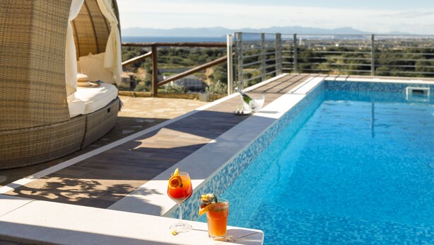 Zona de piscina con una silla lounge de mimbre, dos bebidas sobre una mesa y vistas al paisaje.