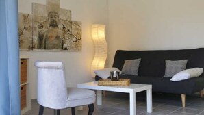 Una sala de estar moderna con un sofá oscuro, un sillón blanco y una mesita de centro blanca. Hay una obra de arte colgada en la pared sobre el sofá y una lámpara de pie a su lado.