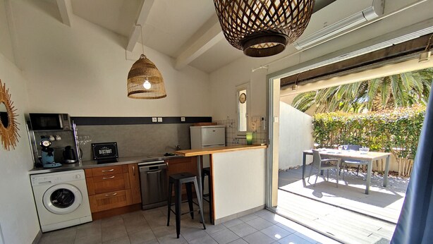 Una cocina moderna con lavadora, cafetera y zona de comedor con mesa y sillas.