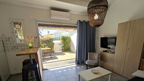 Un espacio habitable compacto con kitchenette, comedor, zona de estar con sofá y televisión, y vista al exterior.