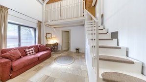 Un vaste espace de vie comprenant un canapé rouge, une table à manger avec des chaises, un escalier et une grande fenêtre avec des rideaux.