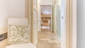 Un couloir étroit, avec un lit sur la gauche, une cheminée au fond et une porte sur la droite.