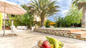 Un espace aménagé au bord de la piscine, avec un mur en pierre, des chaises longues et un saladier rempli de fruits.