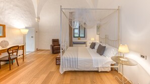 A bedroom with a four-poster bed, a desk with a chair, a small table, and a chair. - Pool house in the park, 7km from the sandy beaches (C) (Patù)