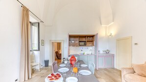 A dining area with a table set for four, a kitchen in the background, and a sofa to the right. - Pool house in the park, 7km from the sandy beaches (C) (Patù)