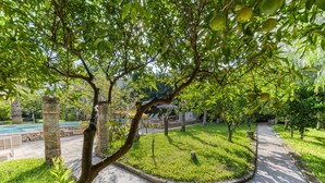 A landscaped garden with a curved pathway, stone pillars, and a pool area in the background. - Pool house in the park, 7km from the sandy beaches (C) (Patù)