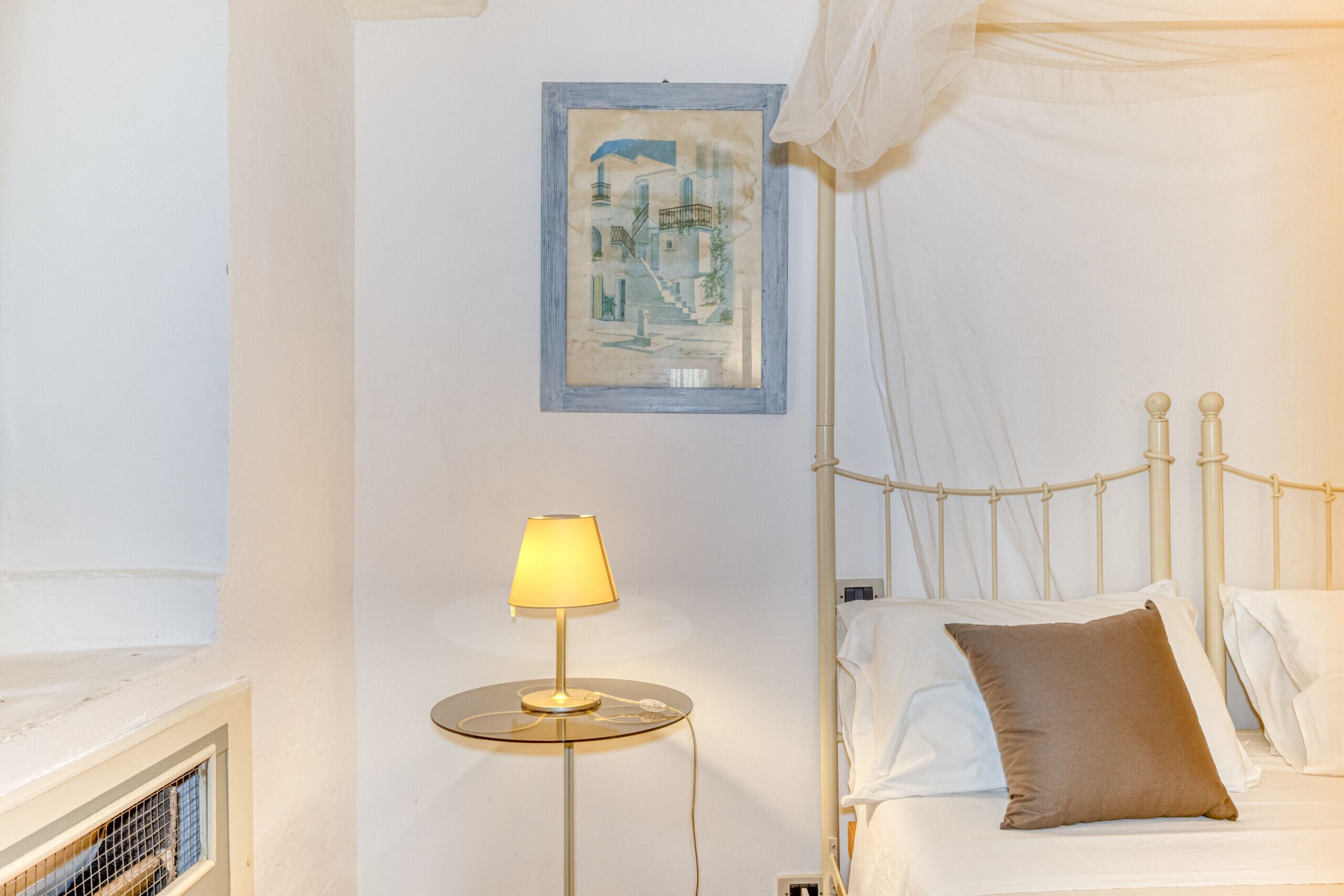 Une chambre à coucher avec un lit, une lampe de chevet, un tableau encadré au mur et une fenêtre avec un rideau.