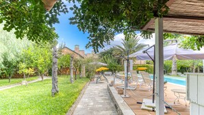 A stone pathway leading to a pool area with umbrellas and lounge chairs. - Pool house in the park, 7km from the sandy beaches (C) (Patù)