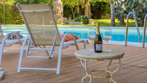 A poolside area with lounge chairs and a table with a bottle and glass. - Pool house in the park, 7km from the sandy beaches (C) (Patù)