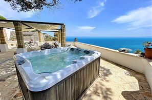 Un bain à remous avec un revêtement extérieur en pierre, une pergola, du mobilier d’extérieur et une vue sur la mer.