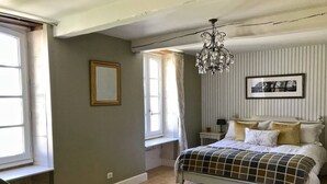 Een slaapkamer met een bed, een raam, een kroonluchter en een ingelijst schilderij aan de muur.