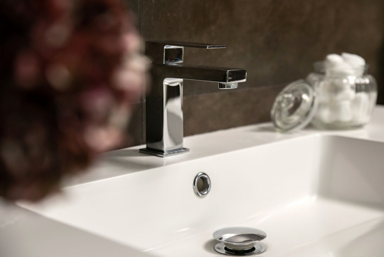 A modern bathroom with a white sink, chrome faucet, and a glass jar with white items on the counter.