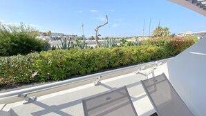 Ein Balkon mit Blick auf eine angelegte Grünfläche, darunter verschiedene Pflanzen und eine Straße im Hintergrund.