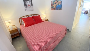 Ein Schlafzimmer mit einem Bett, zwei roten Kissen, einem Nachttisch mit einer Lampe und zwei Wandbildern.