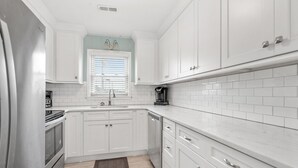 Una cocina moderna con armarios blancos, un refrigerador de acero inoxidable, una cafetera y una ventana con persianas.