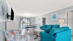 Una sala de estar con un sofá azul verdoso, un sillón estampado y un comedor con una mesa y sillas blancas.