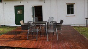 A patio with a table and chairs, a green door, and a white wall with a window. - Idyllic apartment with a view of the water (Preußisch Oldendorf)