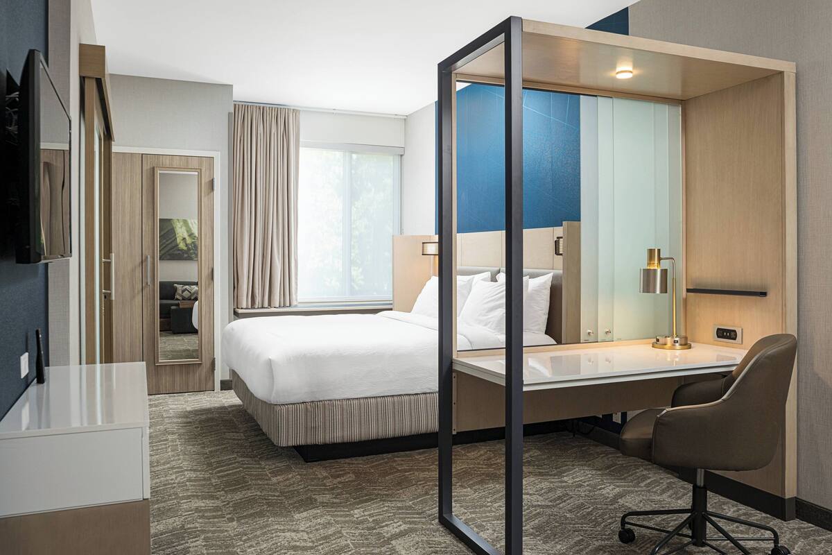 Une chambre d’hôtel avec un lit, un bureau, une chaise et un grand miroir.