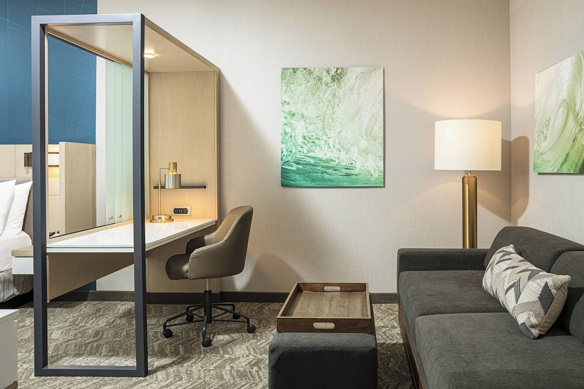 Une chambre d’hôtel équipée d’un bureau, d’une chaise, d’un canapé, d’une lampe et décorée avec des œuvres d’art aux murs.