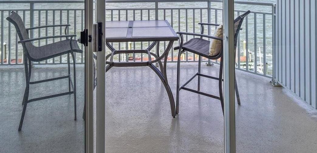 Un balcón con una mesa y dos sillas, vistas al agua y una barandilla.