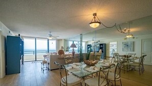 A spacious living room with a glass dining table, comfortable seating, and a view of the ocean. - Seychelles 1405 - Daytona Beach Oceanfront Vacations, Inc (Daytona Beach Shores)