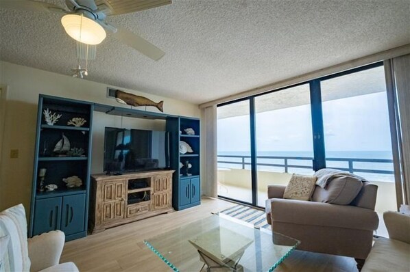 A living room with a large window, a ceiling fan, and a television on a wooden cabinet.