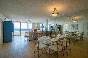 A spacious living room with a glass dining table, comfortable seating, and a view of the ocean.