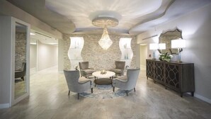 A modern living room with a round coffee table, two armchairs, a chandelier, and a console table with lamps. - Seychelles 1405 - Daytona Beach Oceanfront Vacations, Inc (Daytona Beach Shores)