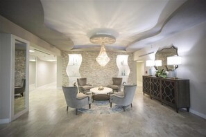A modern living room with a round coffee table, two armchairs, a chandelier, and a console table with lamps.
