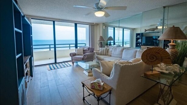 A spacious living room with a large glass door leading to a balcony overlooking the ocean. - Seychelles 1405 - Daytona Beach Oceanfront Vacations, Inc (Daytona Beach Shores)