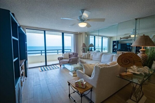 A spacious living room with a large glass door leading to a balcony overlooking the ocean.