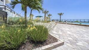A paved outdoor area with a pool, palm trees, and a clear sky. - Seychelles 1405 - Daytona Beach Oceanfront Vacations, Inc (Daytona Beach Shores)