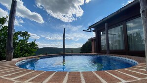 Ein Schwimmbecken mit Ziegelbordstein, umgeben von einer Holzdielen-Terrasse und einem Gebäude mit großen Fenstern.