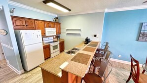 Une cuisine avec des meubles de rangement en bois, un réfrigérateur blanc, un four à micro-ondes et une cuisinière. On y trouve également un coin repas avec une table et des chaises.