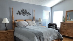 Una camera da letto con un letto di legno, due comodini con lampade, un comò e una sedia.
