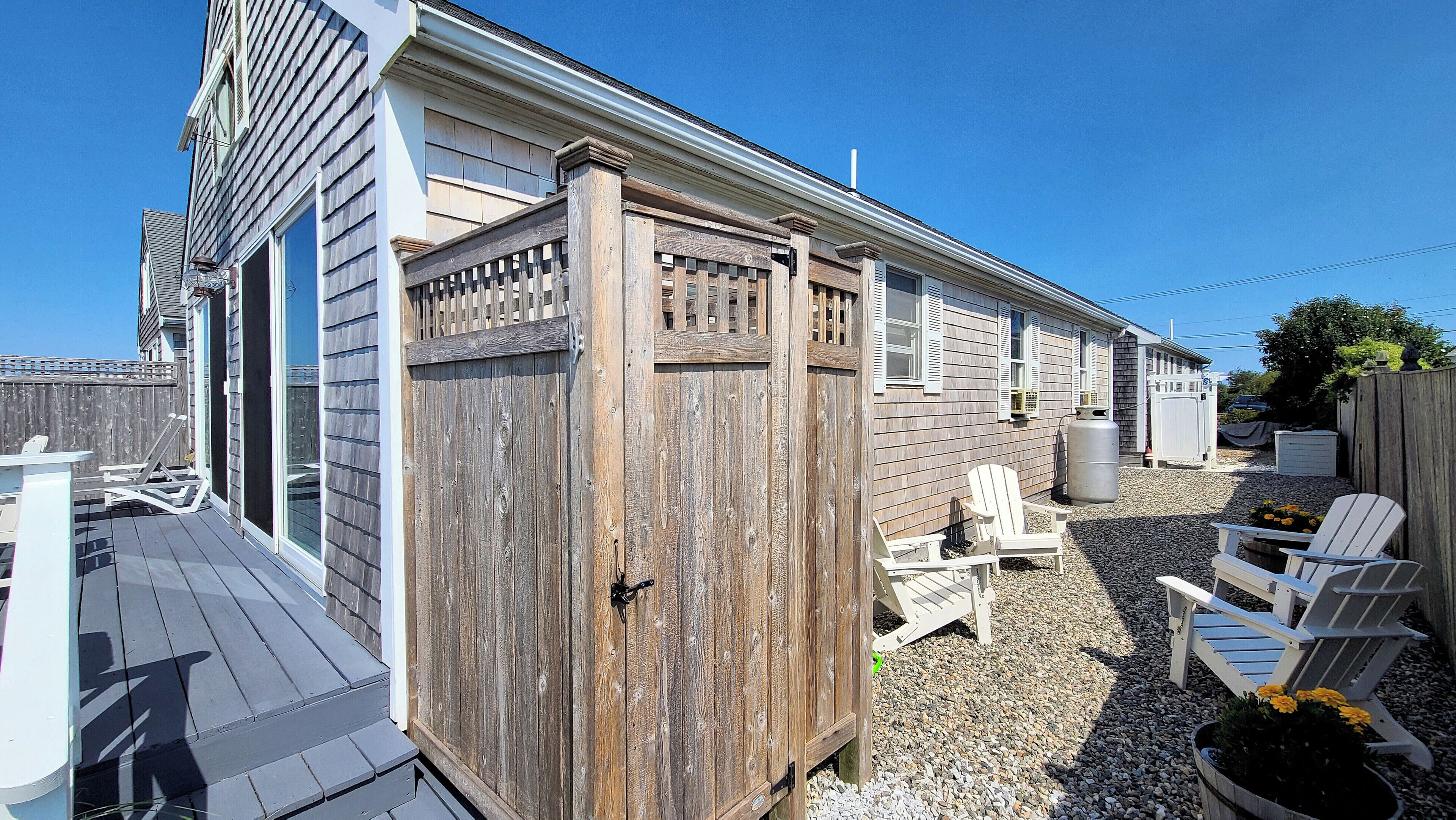 A wooden deck with Adirondack chairs, a grill, and a large water tank.