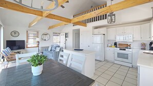 A spacious kitchen with white cabinets, a central island, and a dining area with a dark wooden table and chairs. - Waterfront 2BD Cottage: RIGHT ON THE BEACH, Water View, Direct Beach Access, A/C & Exclusive Use Deck (North Truro)