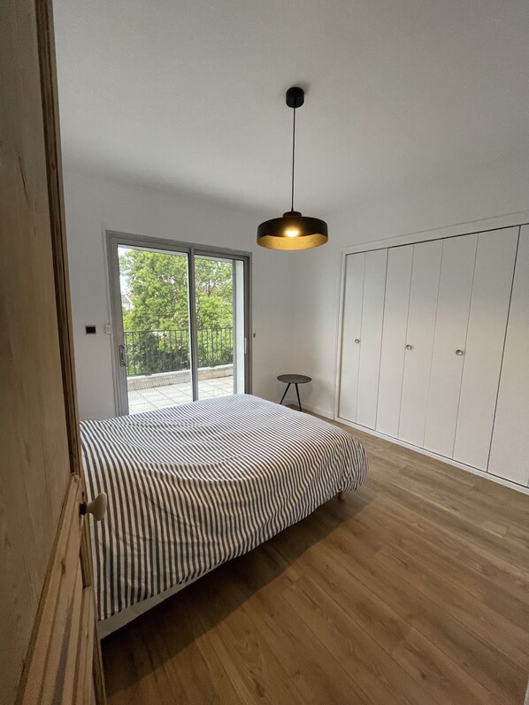 Un dormitorio con cama, armario, una mesita y una lámpara colgante.