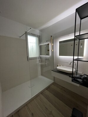 Une salle de bain moderne avec une douche à parois de verre, un grand miroir et un plancher en bois.